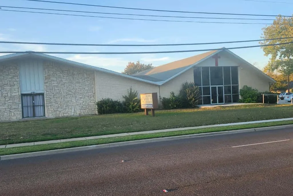 Agape International Church seen from East Parker Road: a low brick building with a red cross on the gable end, a tall glass entrance, and the church sign standing on the front lawn