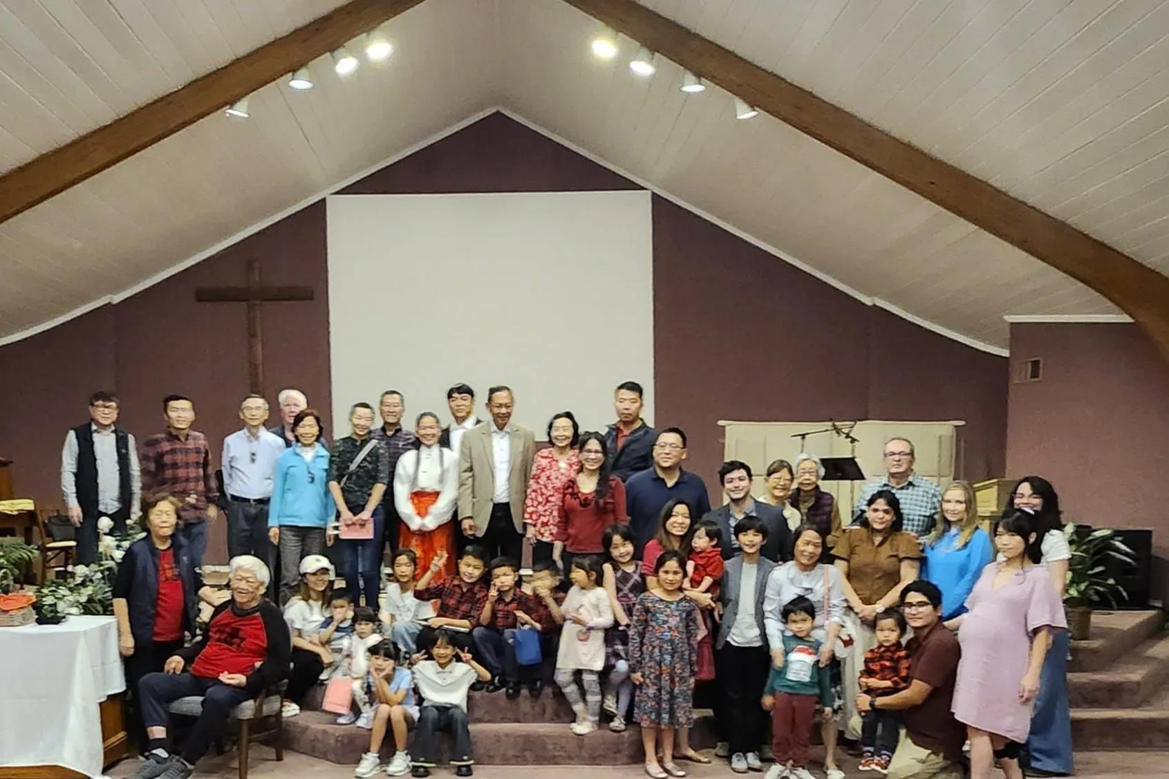 The congregation of Agape International Church gathered together on the platform steps beneath the sanctuary’s vaulted ceiling and wooden cross, with small children seated at the front and adults and grandparents standing behind