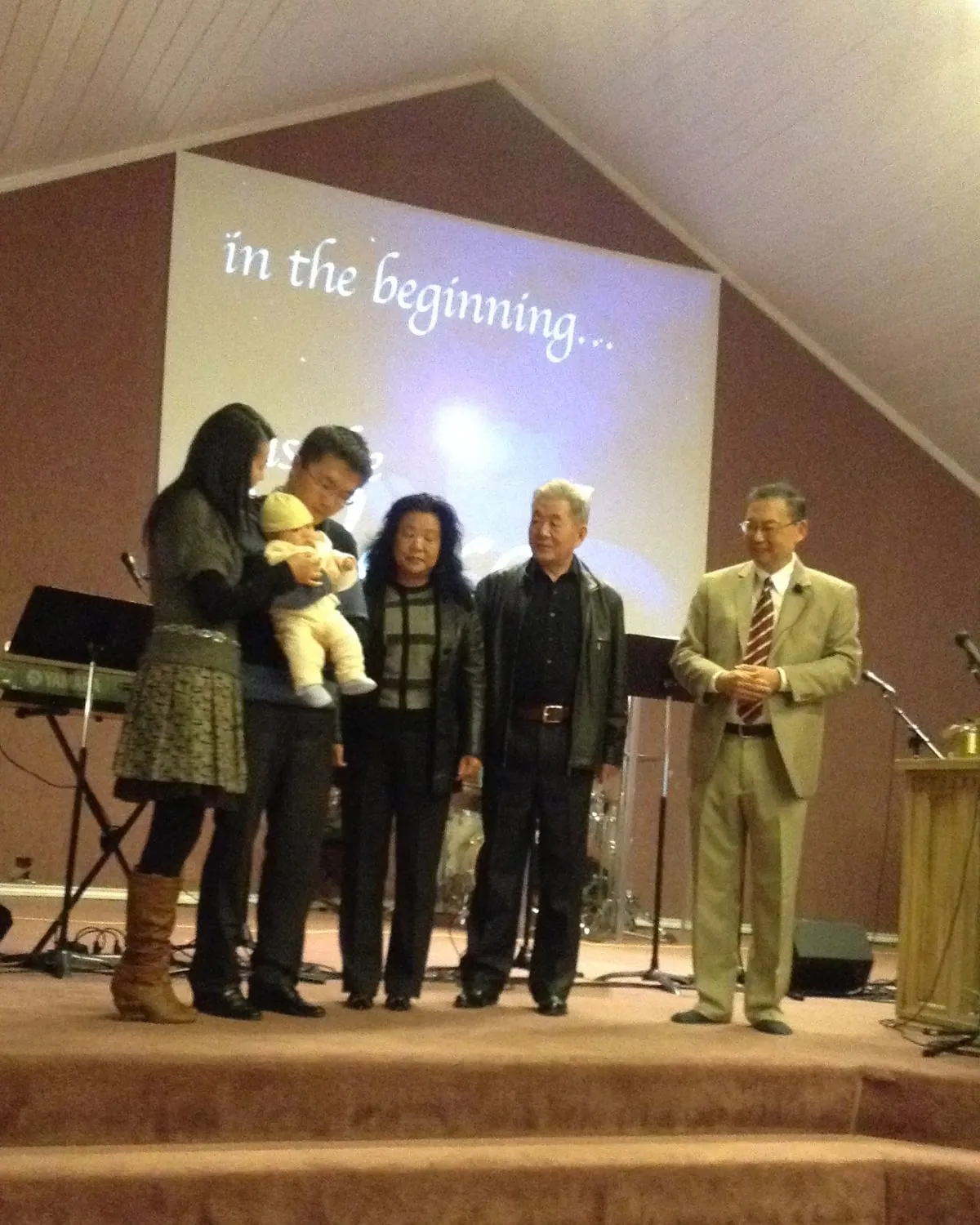 Three generations of one family standing together on the platform with Pastor Daniel S. Chen, the youngest held in his father’s arms