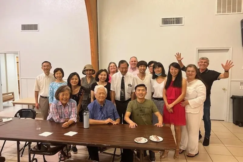 Members of the church gathered around a table in the fellowship hall after a shared meal, smiling together