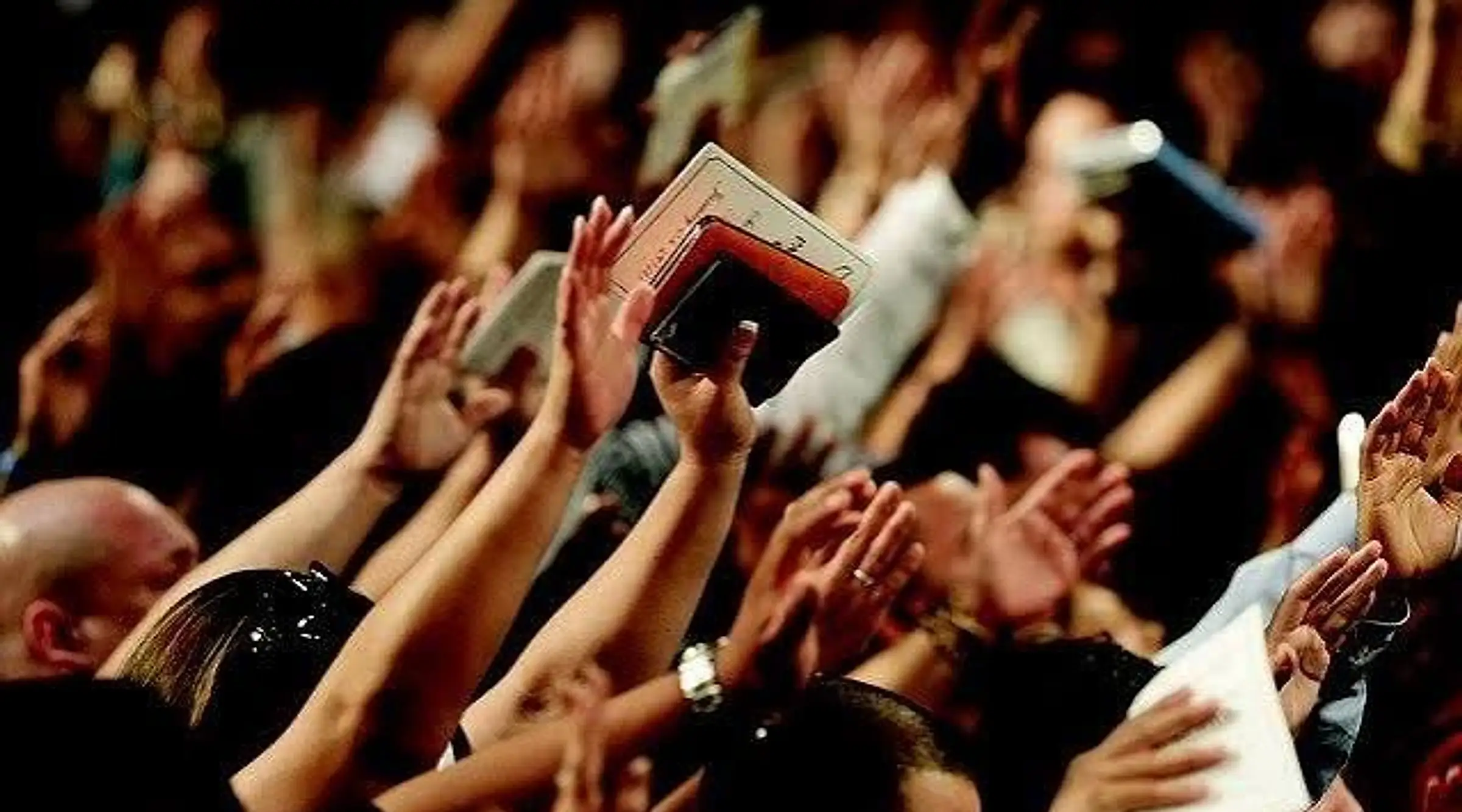 Hands raised in worship above a crowd, one person holding an open Bible up among them