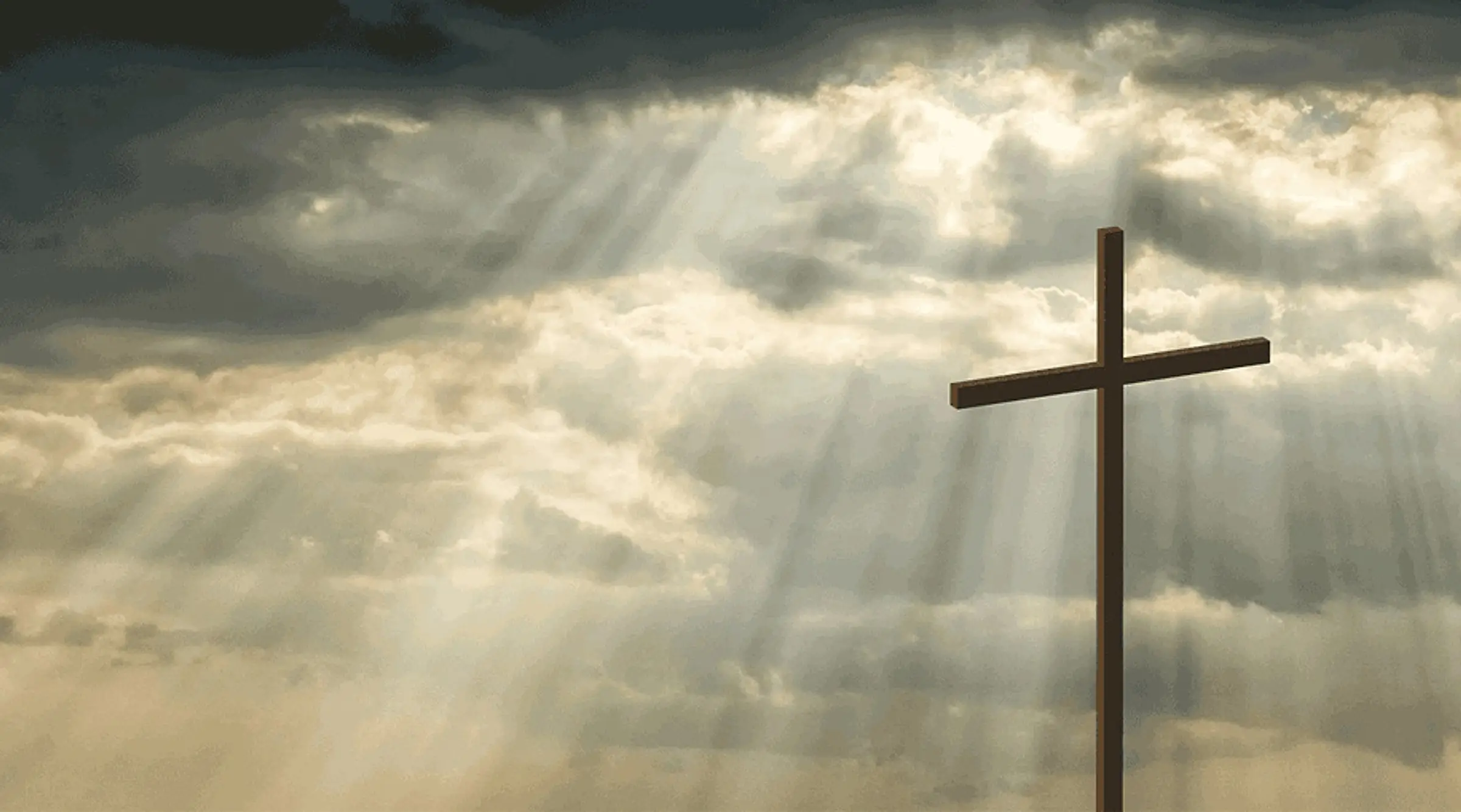 A wooden cross silhouetted against a bank of cloud, with shafts of sunlight breaking through behind it