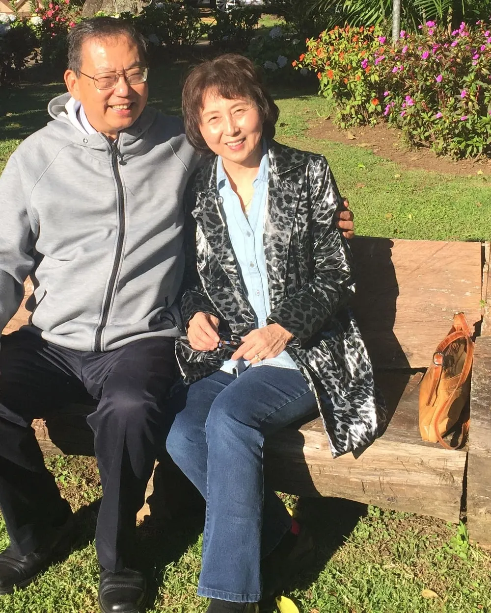Pastor Daniel S. Chen and Mrs. Chen seated together on a wooden bench in a garden, both smiling