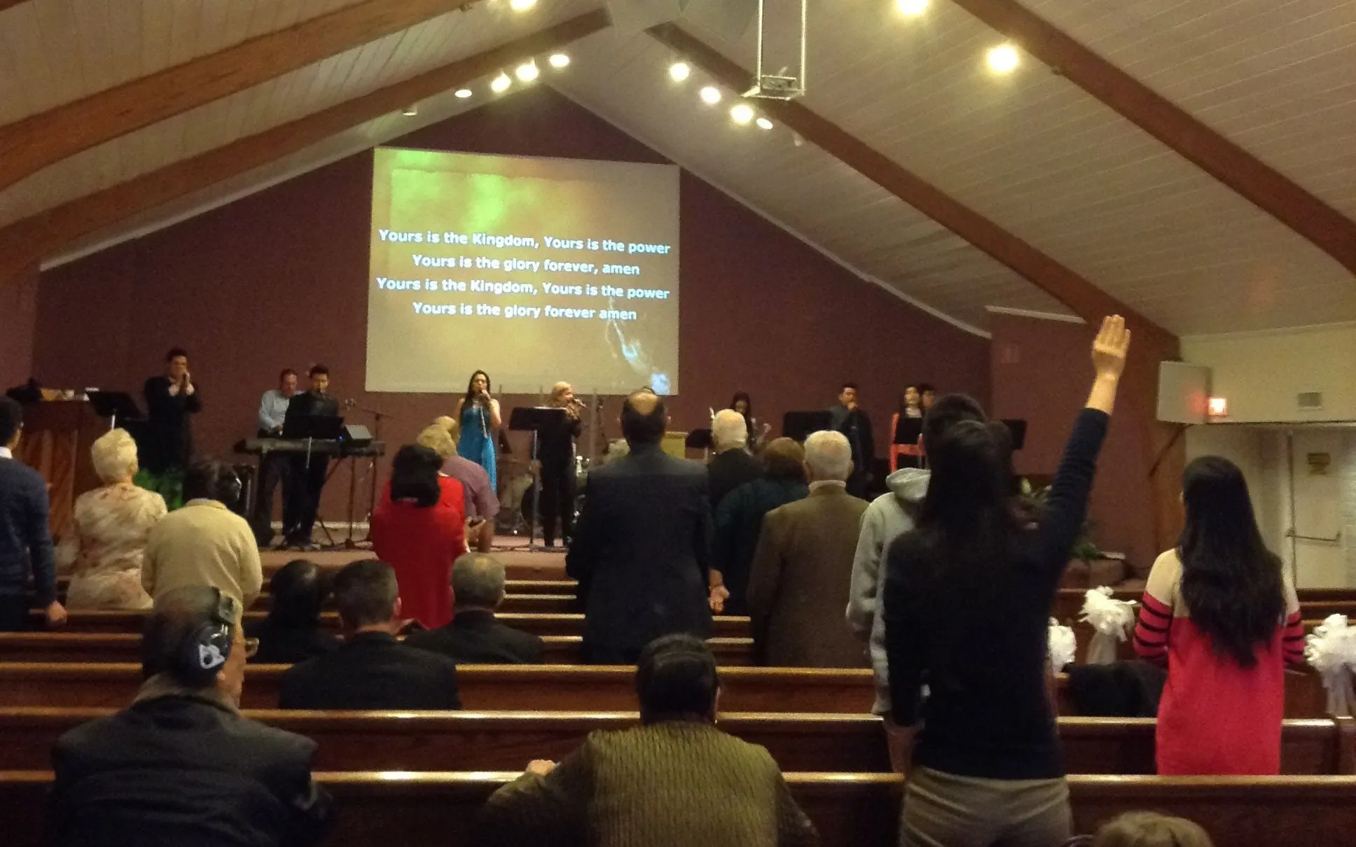 Sunday morning worship at Agape International Church: the congregation standing together, one person with a hand raised, while the worship team leads from the platform beneath the lyric screen